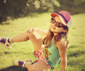 Wall Mural - Fun joying playful kid girl in sunglasses on green glass outdoor summer background. Closeup vintage color