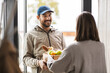 © Syda Productions - food shipping and people concept - happy delivery man giving wooden box with groceries to female customer at home