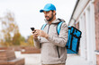 © Syda Productions - food shipping, profession and people concept - happy smiling delivery man with smartphone and thermal insulated bag in city