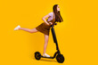 Full length body size view of attractive cheerful girlish girl riding scooter rest hobby isolated over bright yellow color background