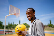 Smiling Young Man With Wireless In-ear Headphones Holding Basketball On Sunny Day