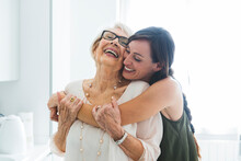 Cheerful Woman Hugging Grandmother In Kitchen At Home