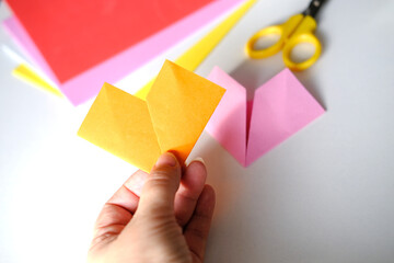 close-up of female hands fold colored paper, makes hearts using origami technique for valentine's day, concept of handmade making and creating gifts for the holiday, valentines