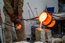 Manual workers pouring molten bronze in container at foundry