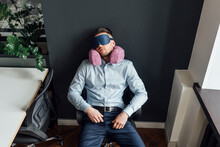 Businessman With Eye Mask And Neck Pillow Resting On Chair In Office