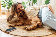 Young Woman With Dog Relaxing On Rug At Home