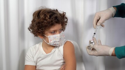 Europe, Italy, Milan - Vaccination against Covid-19 Coronavirus for children in pediatric age 5 to 11 years - pro vax and no vax with generic vaccine vial - Doctor make vaccine to boy with mask