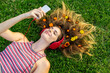 © Westend61 - Smiling young woman with flowers in hair lying on grass listening music through headphones
