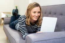 Smiling Woman Using Digital Tablet While Lying On Sofa At Home
