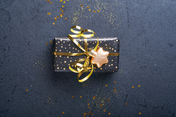 Wall Mural - Holiday gift box or present with ribbon, golden confetti and gold baubles on black background. Magic christmas greeting card. Christmas Decoration. Border design. Mock up. Top view.