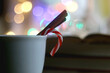 © jelena990 - Cup of warm drink with cinnamon stick and candy cane, open book, reading glasses, lit candles and colorful bokeh lights. Selective focus.