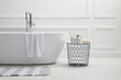 Modern ceramic bathtub and table with toiletries near white wall indoors
