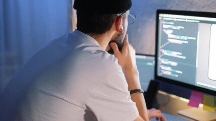 Young man mobile developer writes program code on a computer, programmer work in home office.