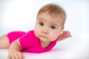 Wall Mural - cute, beautiful little girl in a pink bodysuit
 and a bandage lies on a white background, smiles and gnaws toys. beautiful baby. teeth are erupting. portrait of a baby. portrait of a beautiful girl