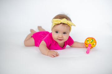 Wall Mural - cute, beautiful little girl in a pink bodysuit
 and a bandage lies on a white background, smiles and gnaws toys. beautiful baby. teeth are erupting. portrait of a baby. portrait of a beautiful girl