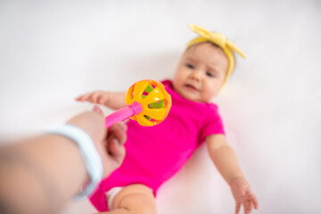 Wall Mural - cute, beautiful little girl in a pink bodysuit
 and a bandage lies on a white background, smiles and gnaws toys. beautiful baby. teeth are erupting. portrait of a baby. portrait of a beautiful girl