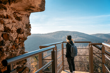 Wall Mural - Young woman traveler with backpack enjoying mountain view from observation deck at sunset