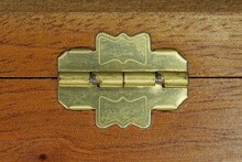 One Small Yellow Brass Hinge On A Brown Wooden Box Board