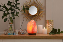 Himalayan salt lamp, candles and crystals on table near white wall indoors