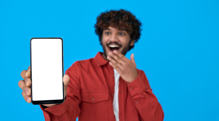 Happy excited surprised young indian man holding cellphone showing big white blank empty mockup screen advertising betting app on phone isolated on blue background. Cell wow application advertisement