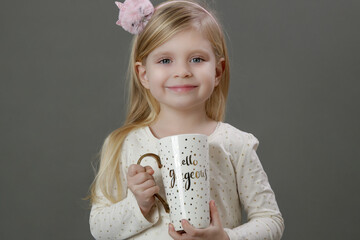 Studio portrait of adorable blonde toddler girl holding ceramic mug.