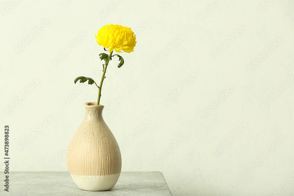 Vase with yellow chrysanthemum flower on table against light wall
