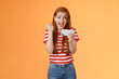 Happy excited redhead female pass level, like awesome game, score goal, hold smartphone horizontally, fist pump success, celebrate lucky achievement, smiling broadly, orange background