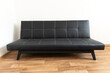 © dechevm - Modern black leather convertible sofa bed, wooden floor. Empty waiting room with a modern black sofa
