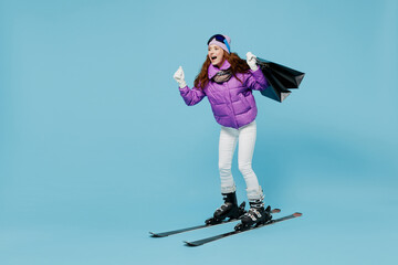 Wall Mural - Full body skier woman in warm purple padded windbreaker jacket ski goggles mask spend weekend in mountains holding package bags with purchases after shopping isolated on plain blue background studio