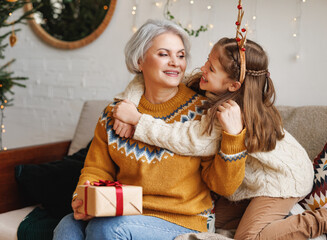 Sticker - Little girl granddaughter giving Christmas gift box to smiling grandmother during winter holidays