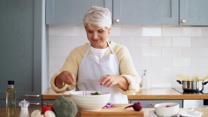 Canvas Print - healthy eating, food cooking and culinary concept - happy smiling senior woman adding red onion to vegetable salad on kitchen