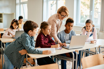 multiracial group of elementary students having computer class with their teacher in classroom.