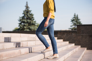 A young, beautiful and attractive Caucasian brunette girl in a yellow sweater climbing up the stairs.