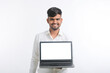 © PRASANNAPIX - Young indian man showing laptop screen with copy space on white background.