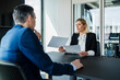 © Westend61 - Businesswoman holding documents while discussing with colleague during meeting in board room