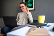 © Westend61 - Smiling woman waving hand to video call on laptop in living room
