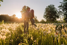 Young Couple Embracing Each Other Standing Amidst Flowers On Meadow During Sunset