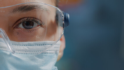 Wall Mural - scientist showing one eye on camera in laboratory, wearing safety glasses and face mask. woman biolo