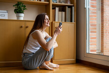 Smiling Woman Using Mobile Phone While Sitting On Floor At Home
