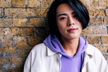 Young Man Wearing Purple Hooded Shirt In Front Of Brick Wall