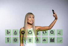 Blond Woman Taking Selfie Through Mobile Phone With Sustainable Icons Against White Background