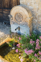 France, Dordogne, Beynac-et-Cazenac, Flowers Blooming In Front Of Small Stone Fountain