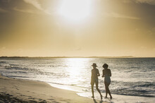 Rear View Of Female Friends Walking At Grace Bay Beach During Sunset, Providenciales, Turks And Caicos Islands