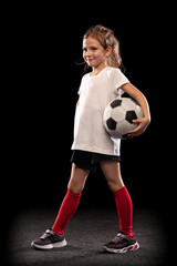 Wall Mural - Portrait of little girl, football player uniform posing isolated over black background