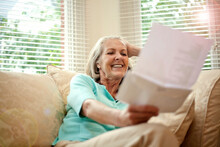 Happy Senior Woman Reading Letter While Sitting On Sofa In Living Room