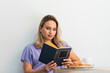 © Westend61 - Beautiful woman reading book in front of wall at coffee shop