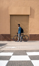 Man With Bicycle Standing By Wall During Sunny Day