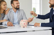 © Studio Romantic - Close up of piggy bank on background of male insurance mortgage broker who gives keys to married couple. Concept of approving mortgage, buying new home or good deal with profit.