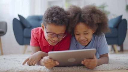 Wall Mural - Cheerful black siblings lying on floor with tablet, having fun together, smiling