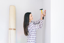 Smiling Woman Hammering Nail In Wall At Home